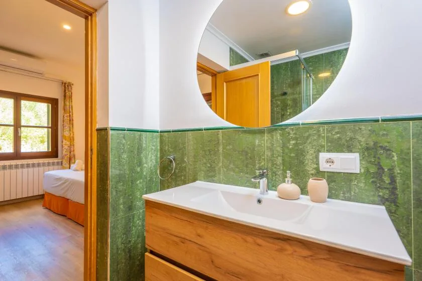A bathroom vanity with a wide mirror and green tiled walls.