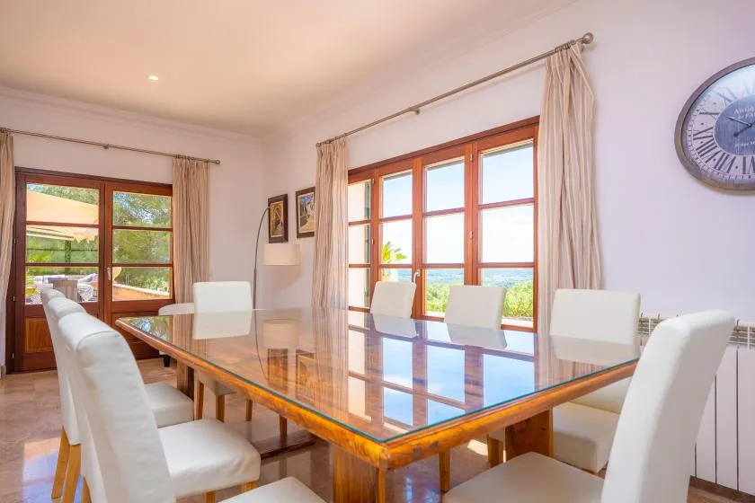 A bright dining room with a large glass-topped table and white seating.