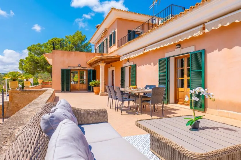 A sunlit patio with outdoor seating and a dining table beside a peach-colored house.