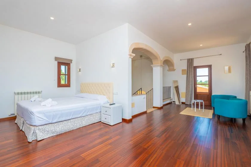 A bright bedroom with a neatly made bed, a small table, and blue seating.