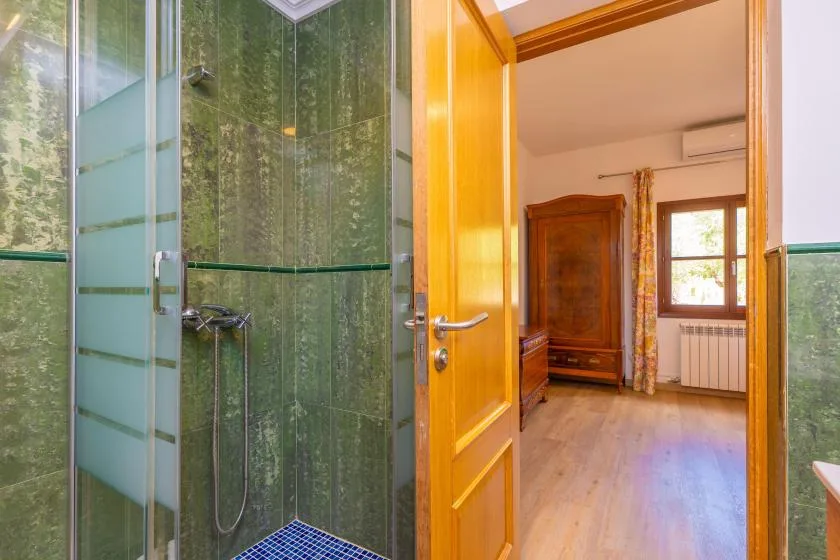 A bathroom shower opens onto a bedroom with a wooden wardrobe and window.