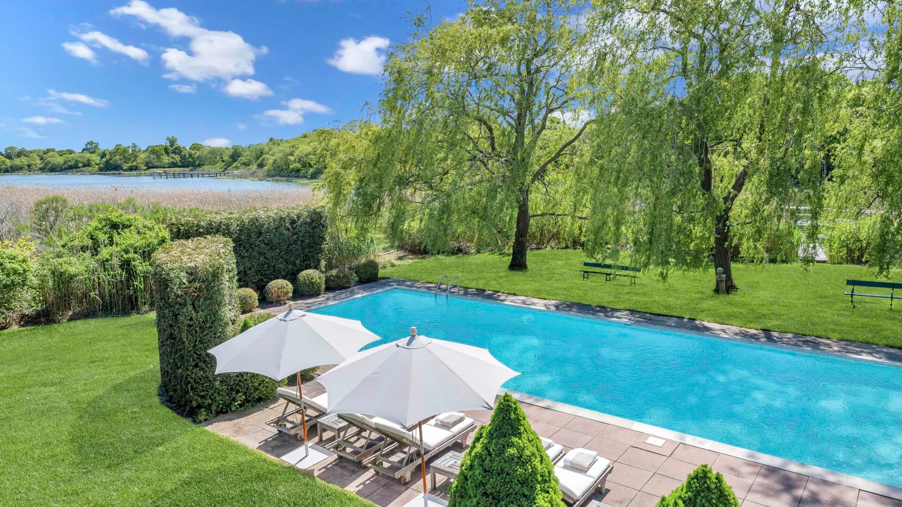 Una piscina al aire libre junto a un césped, con un lago visible más allá del jardín.