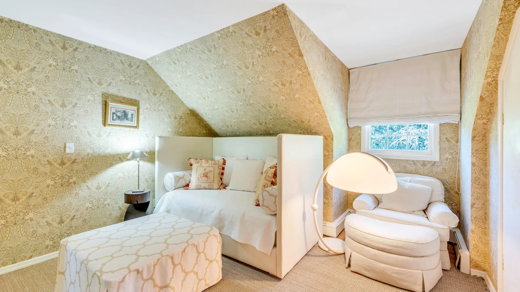 Un dormitorio con una cama, una pequeña zona de estar y paredes con estampado dorado.