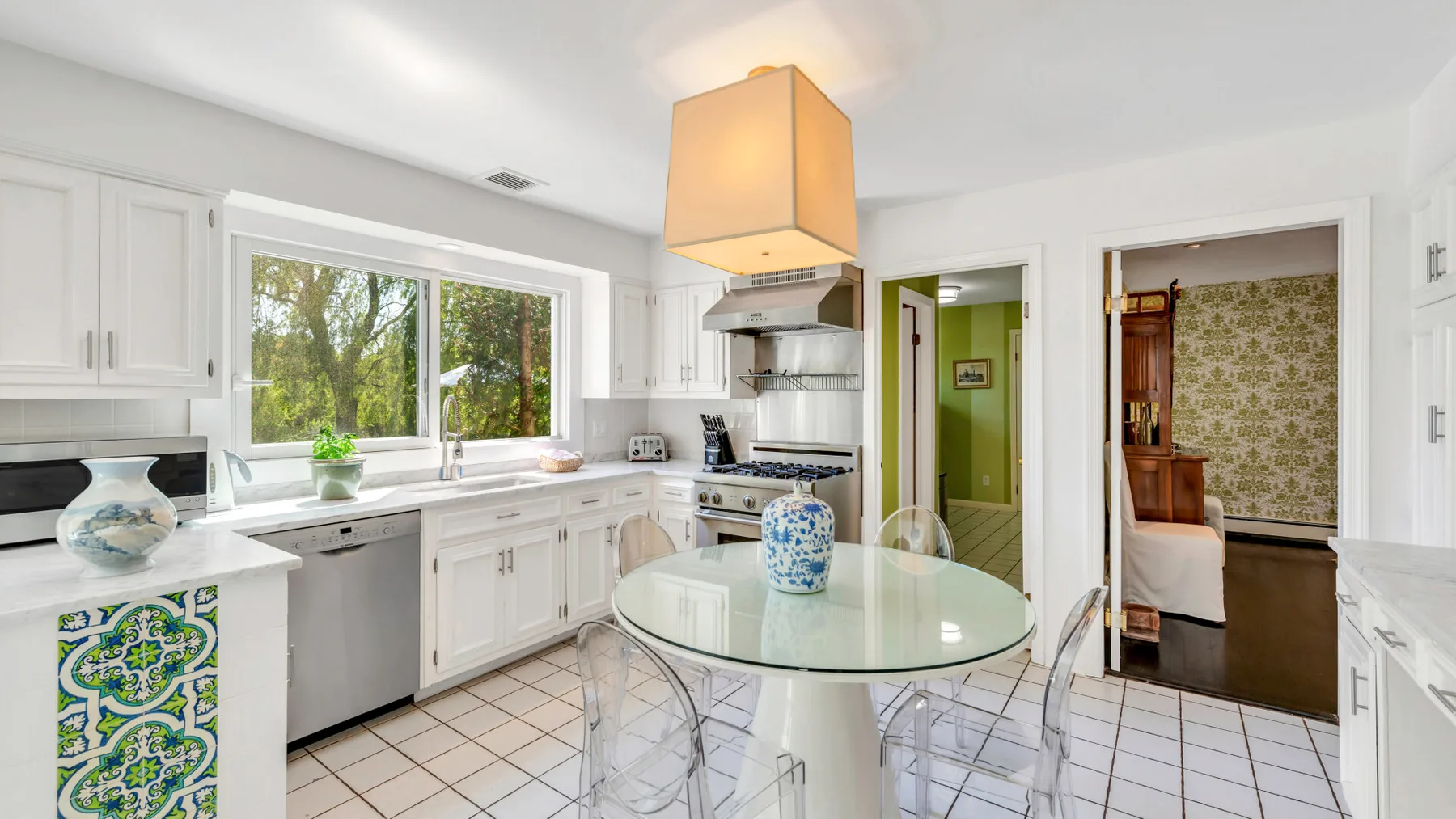 Una cocina blanca y luminosa con una mesa de vidrio y una ventana con vista a los árboles.