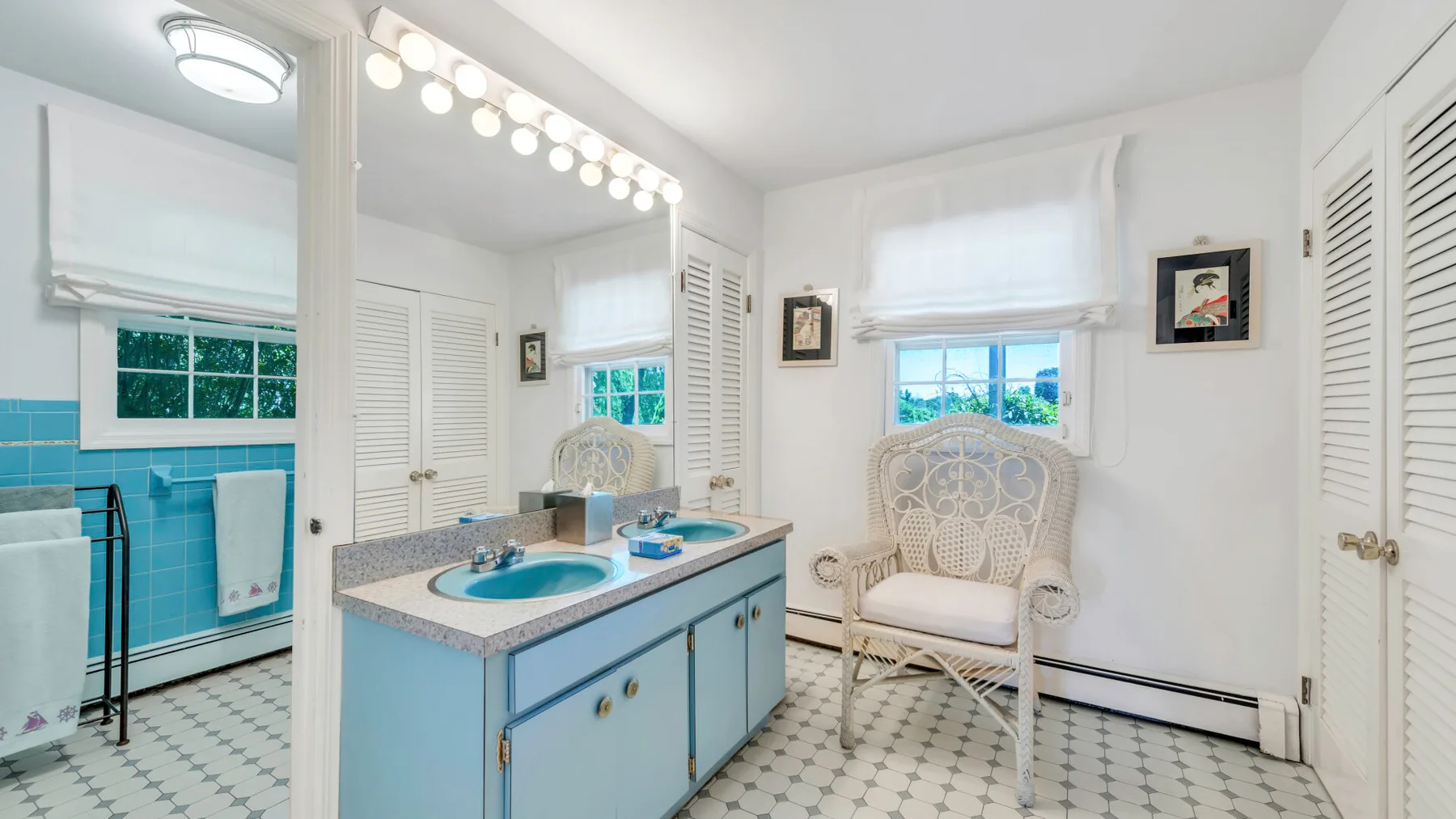 Un baño luminoso con un tocador azul, suelo estampado y una silla acolchada.