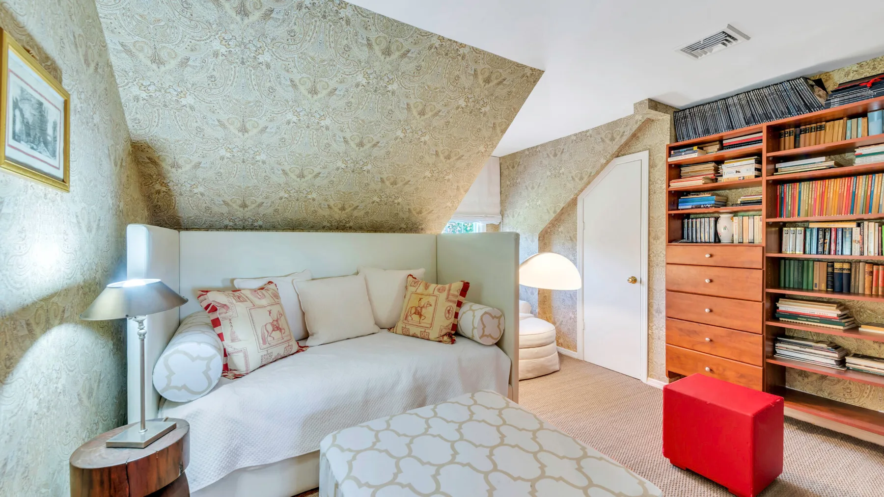 Un dormitorio abuhardillado luminoso con cama, cojines estampados y una estantería empotrada.