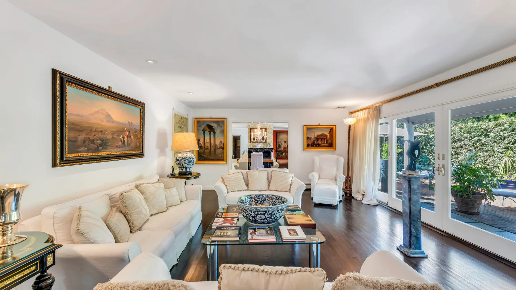A bright living room with seating, framed artwork, and large windows opening onto a patio.