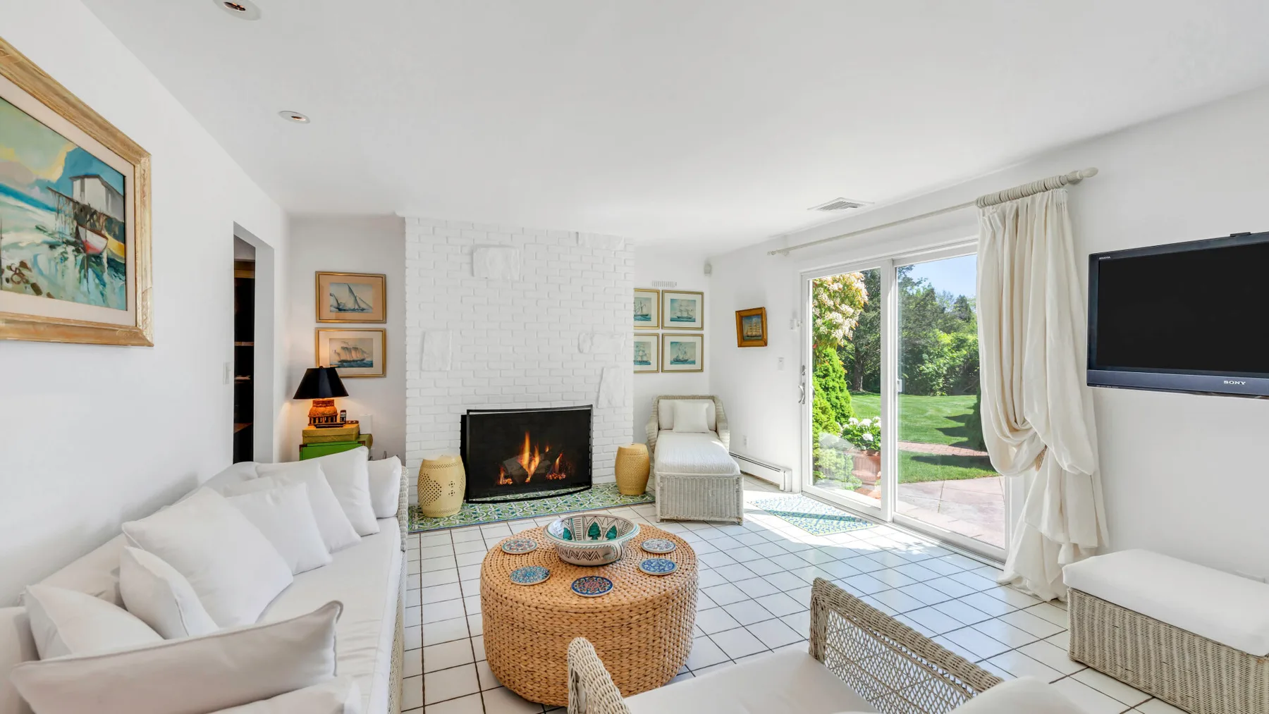 Una luminosa sala de estar con asientos, una chimenea y puertas de vidrio hacia el jardín.