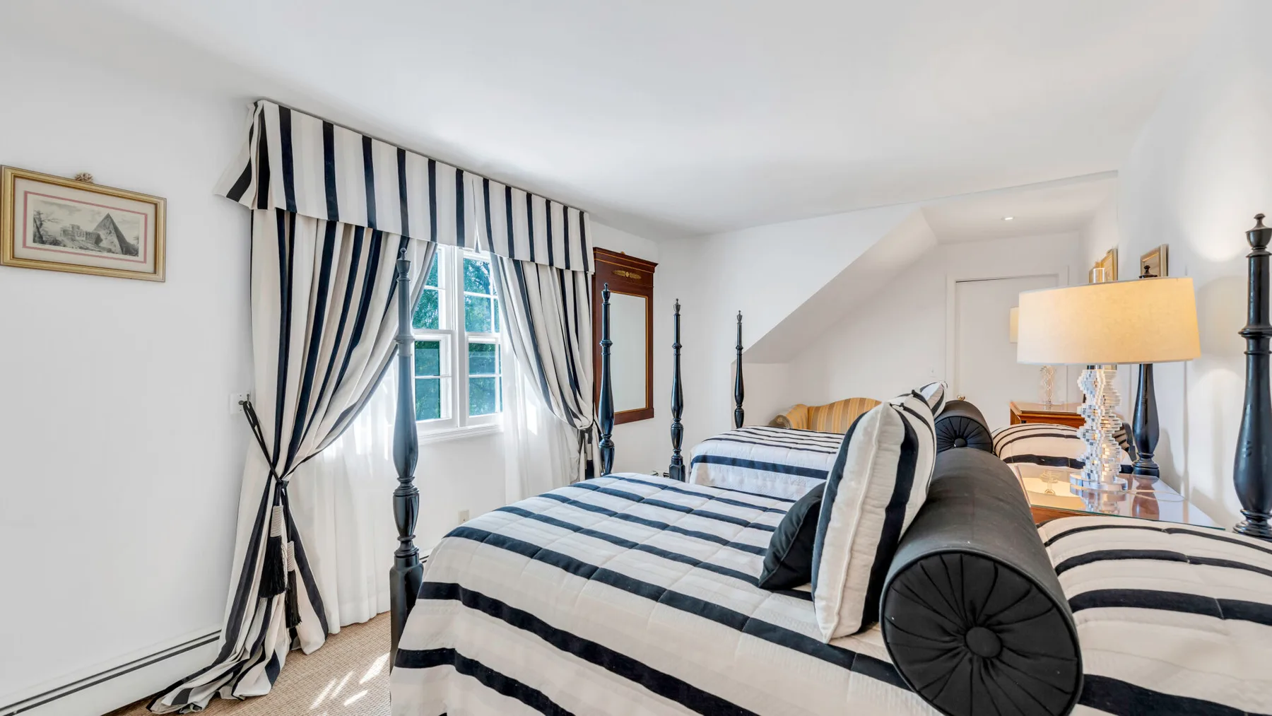 Un dormitorio con ropa de cama a rayas, armazones oscuros y una ventana con cortinas.