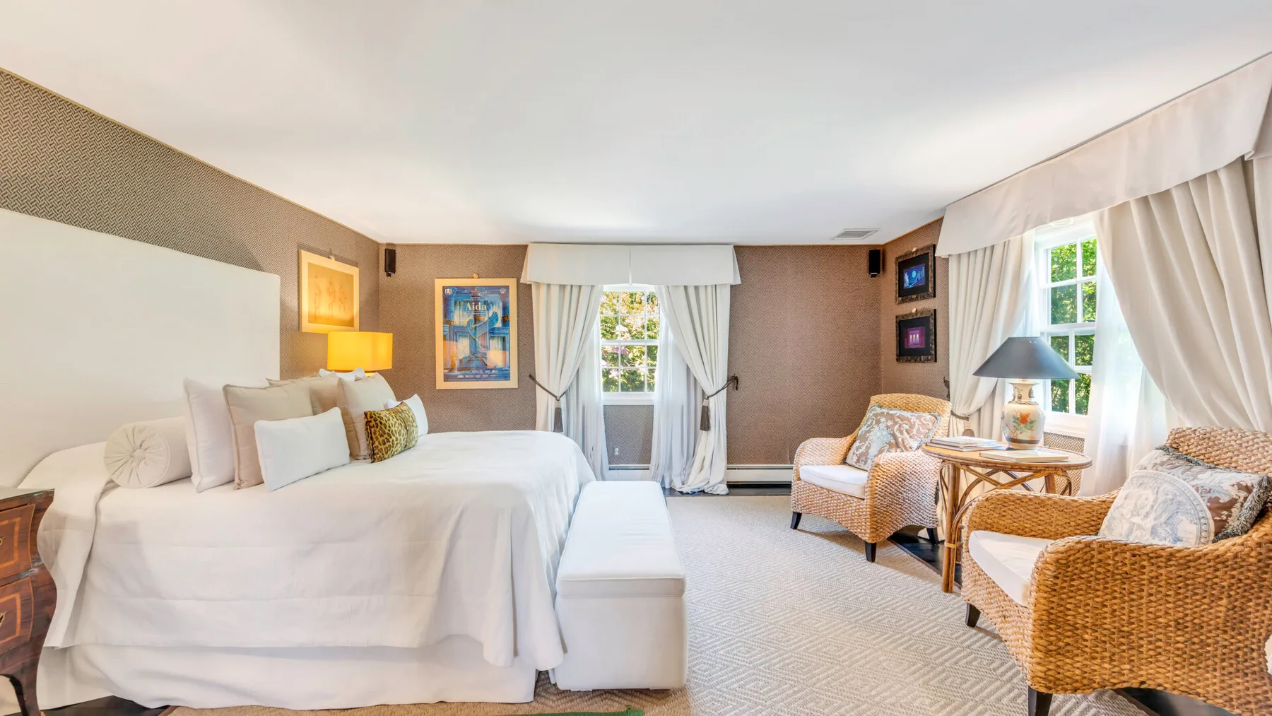 Un dormitorio luminoso con una cama grande y una zona de estar junto a las ventanas.