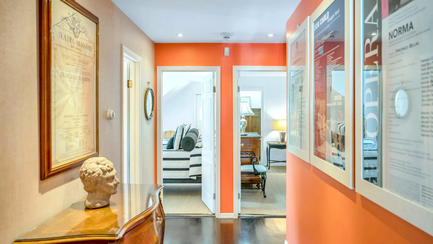 Un pasillo luminoso con cuadros enmarcados y puertas abiertas hacia habitaciones amuebladas.