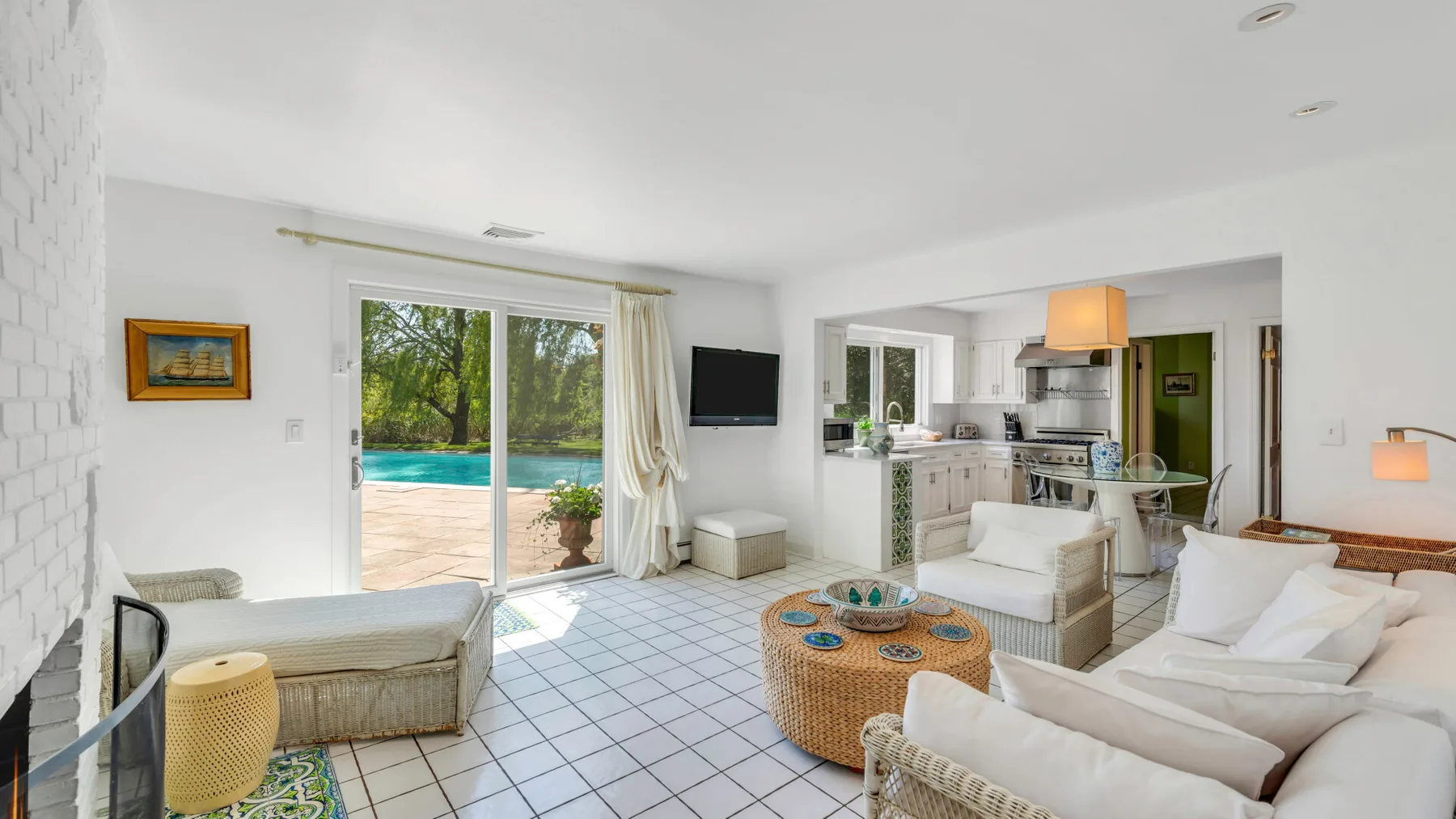Una sala luminosa da a un patio y una piscina, con la cocina al fondo.