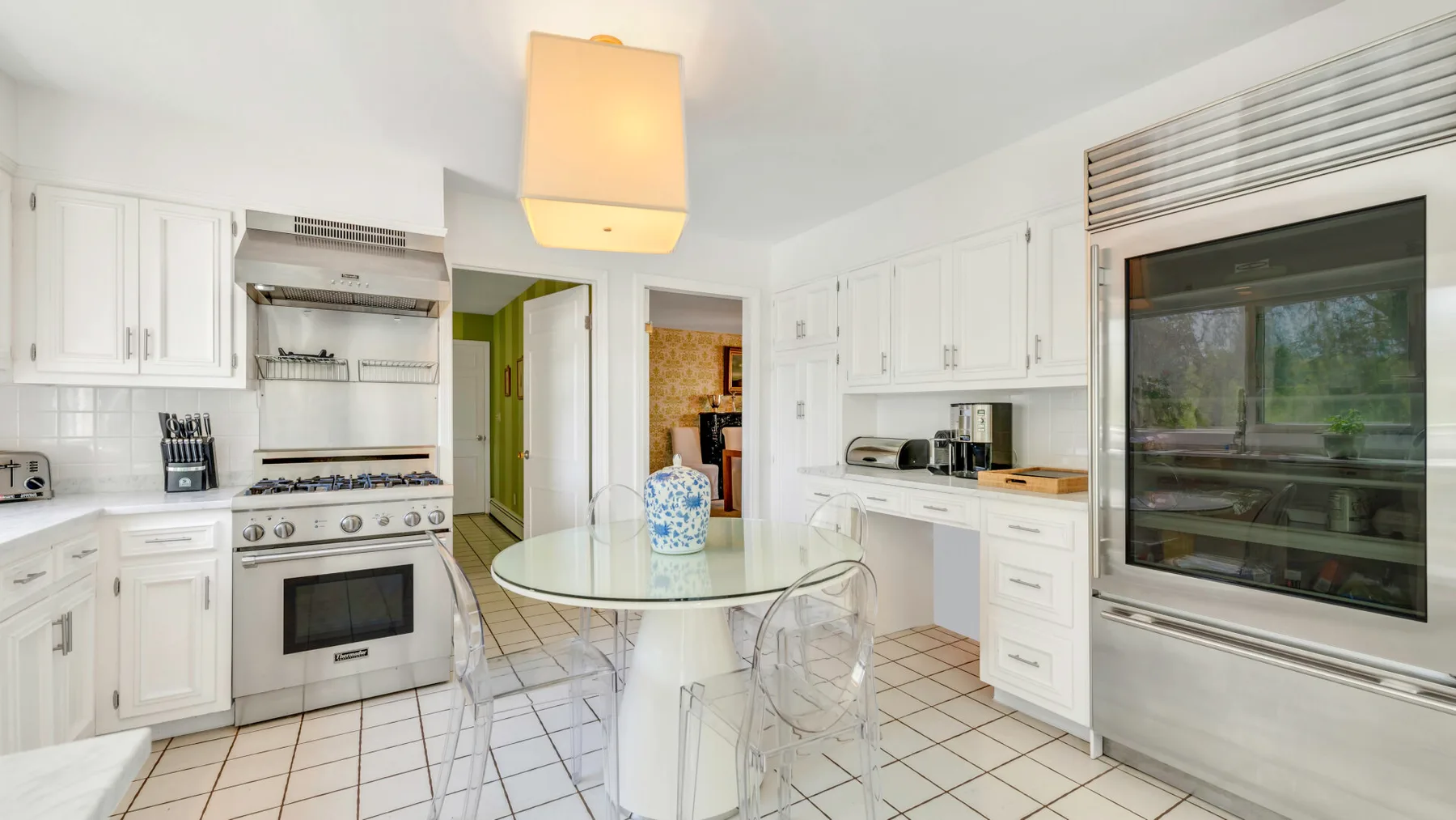 Una cocina blanca y luminosa con una mesa de vidrio y electrodomésticos integrados.