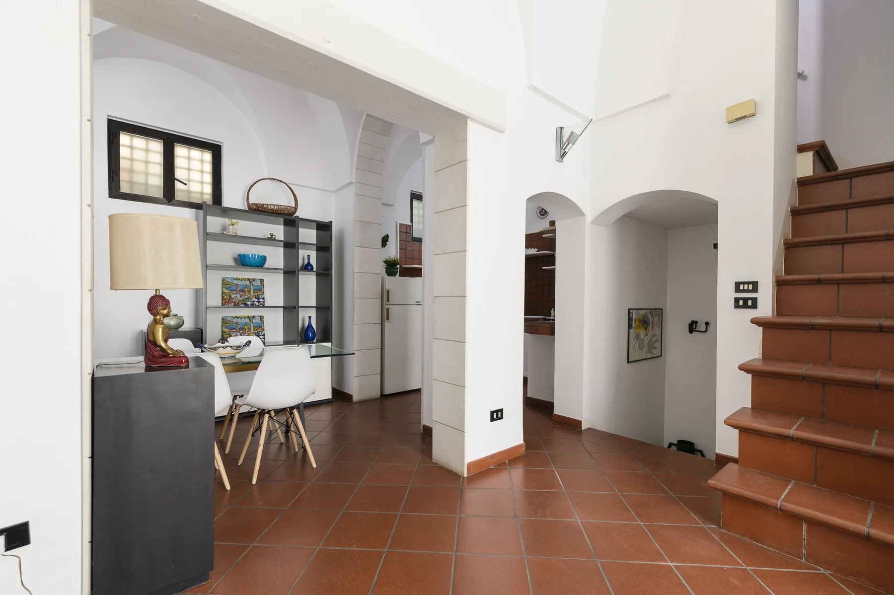 Un interior luminoso con suelo de baldosas, mesa de comedor y escalera.