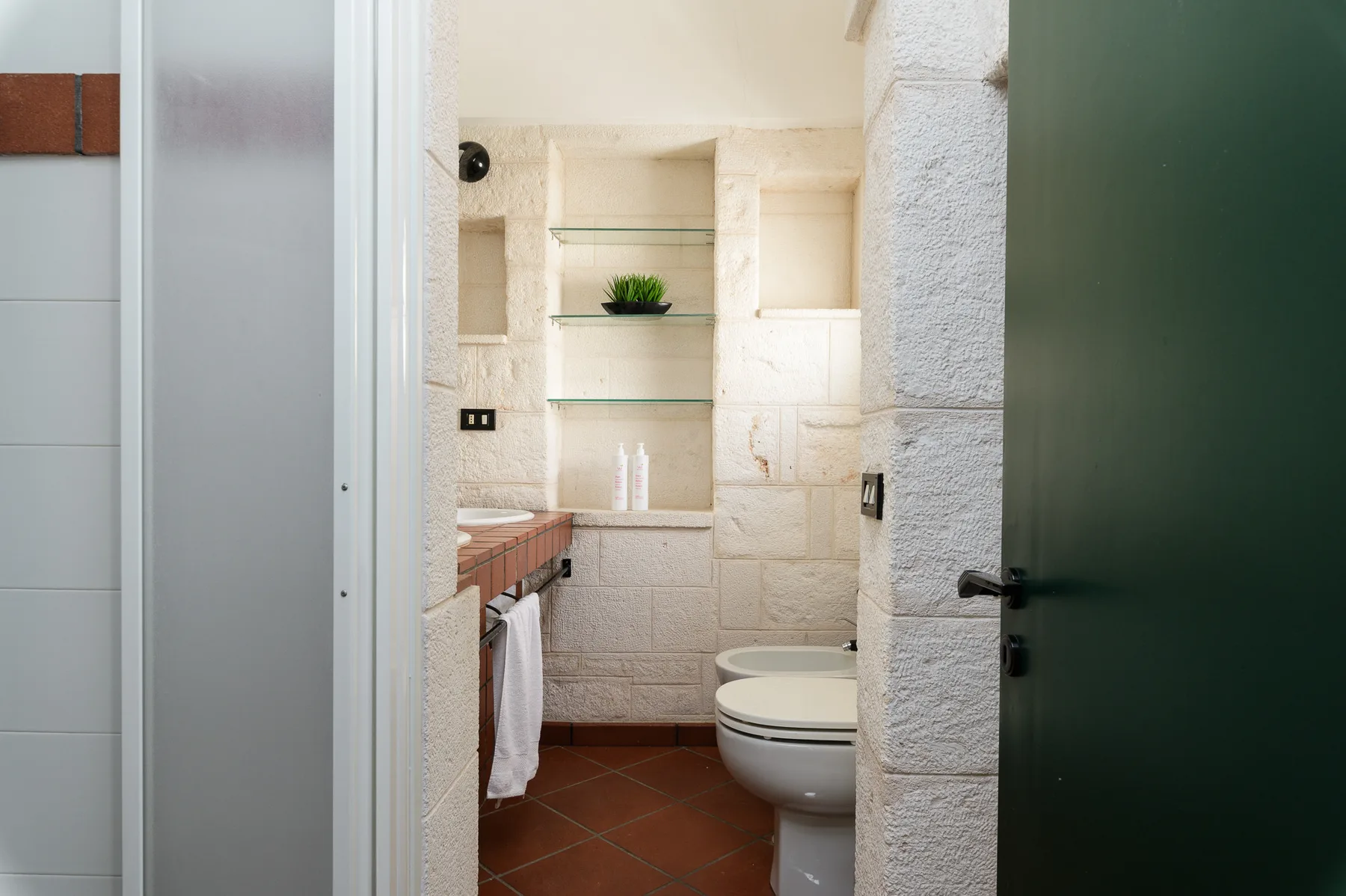 Un baño con inodoro, paredes revestidas y estantes de vidrio.
