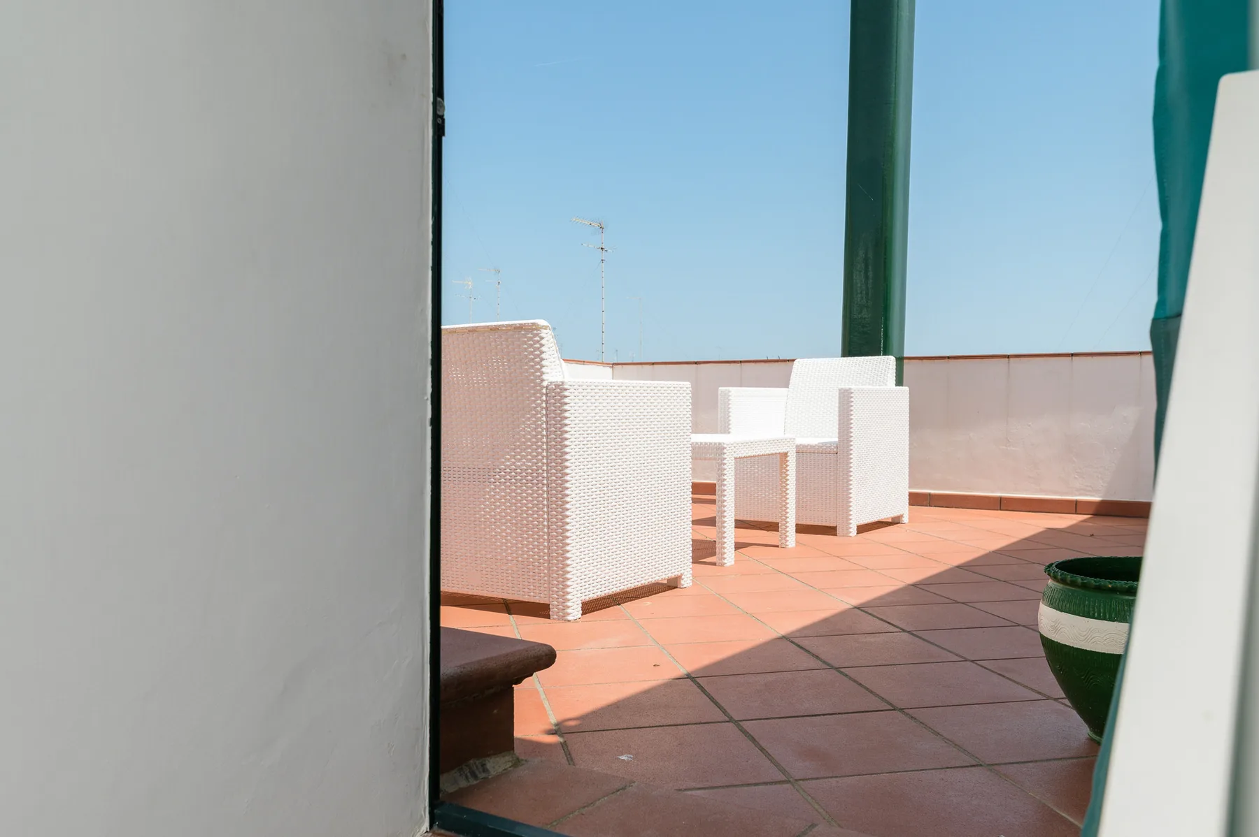 Una terraza soleada con asientos blancos de mimbre y una mesa pequeña.