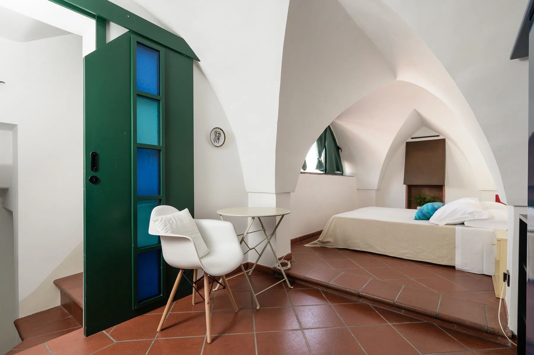 Un dormitorio con una cama elevada, asientos blancos y un techo abovedado.