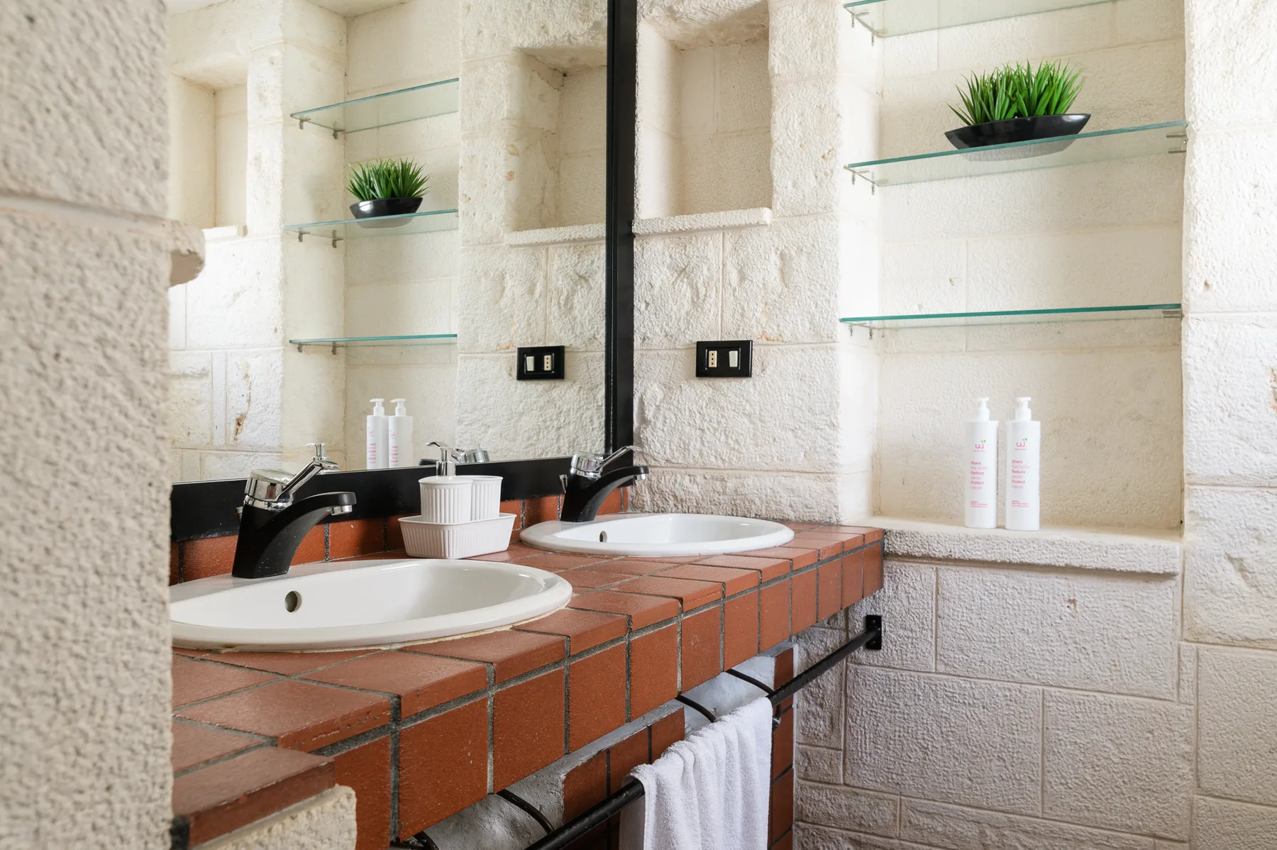 Un tocador de baño con dos lavabos, espejos y estantes de vidrio.