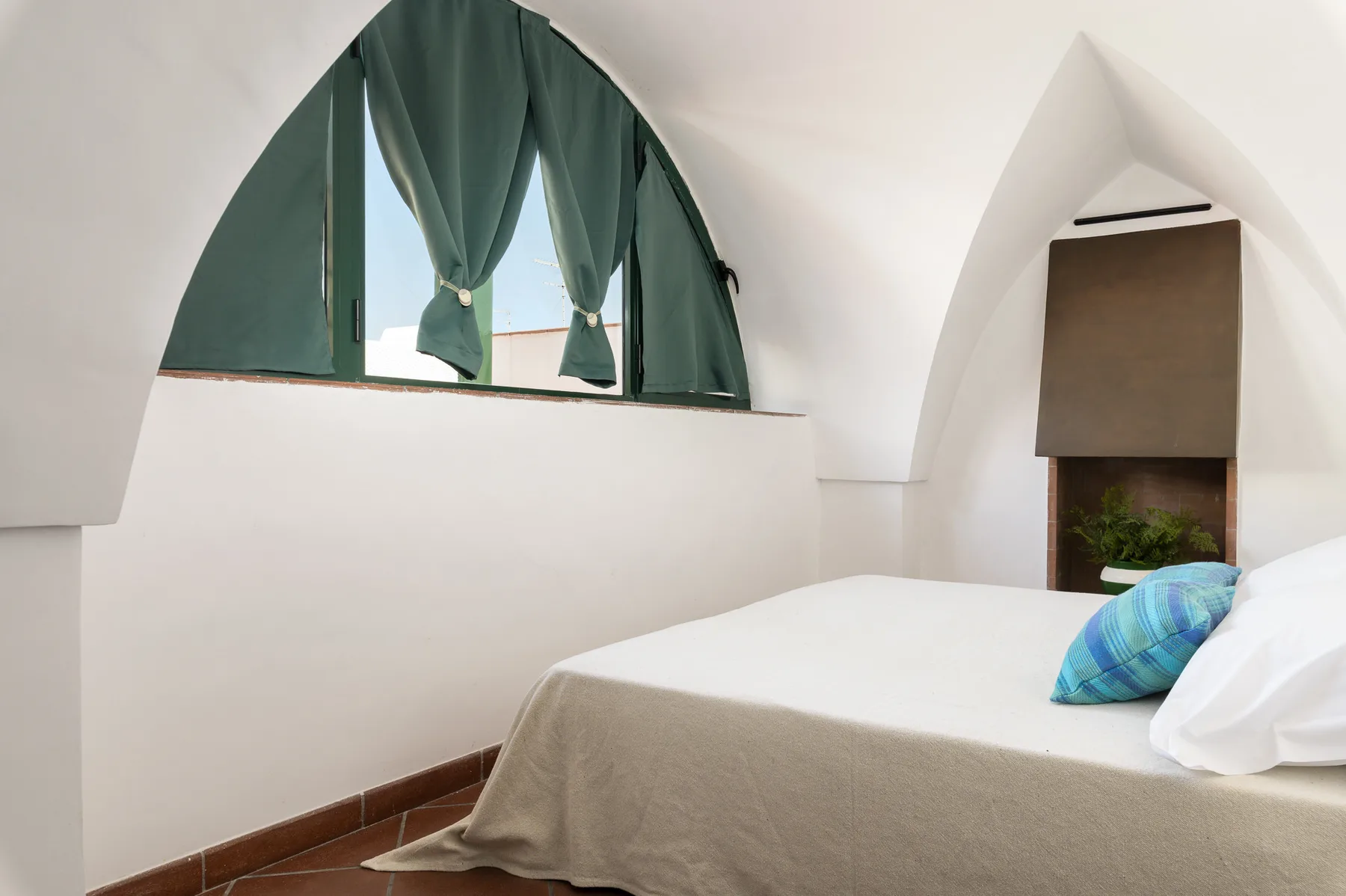 Un dormitorio con una cama bien arreglada y una gran ventana arqueada.