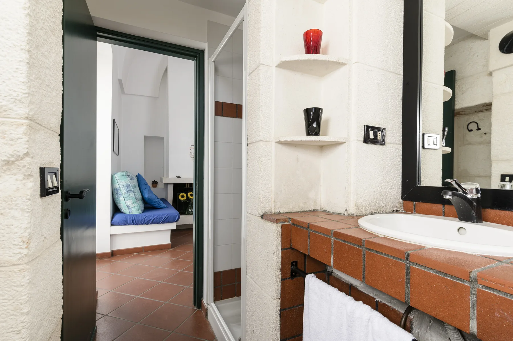 Un baño alicatado con lavabo y una puerta abierta a una pequeña zona de estar.