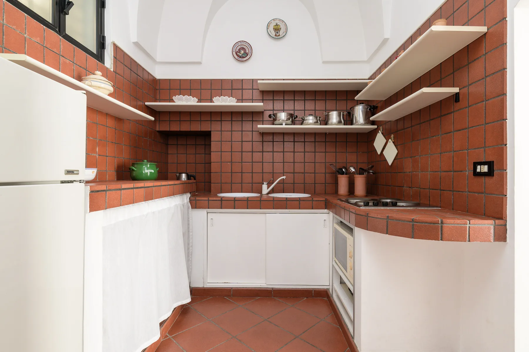 Una cocina compacta con paredes de azulejos color terracota y armarios blancos.