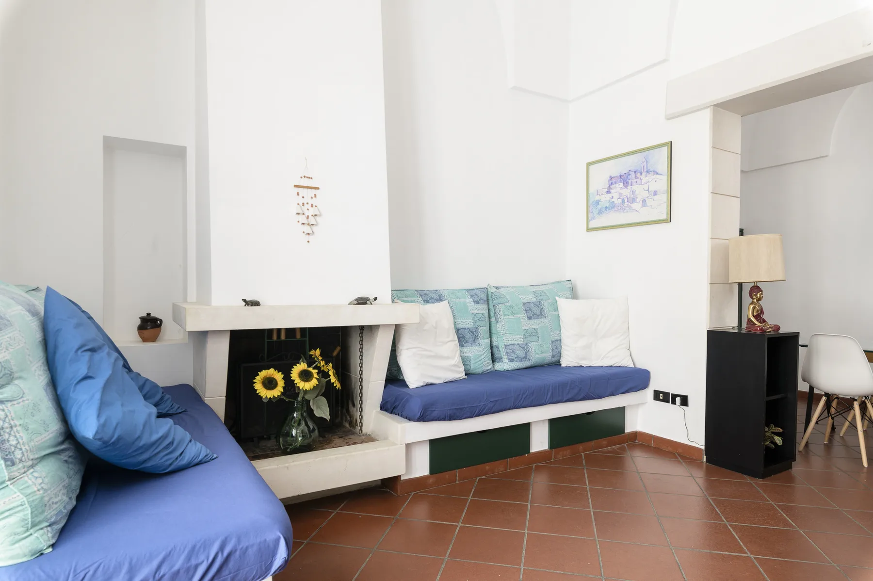 Una sala luminosa con asientos azules, una chimenea y suelo de baldosas de terracota.