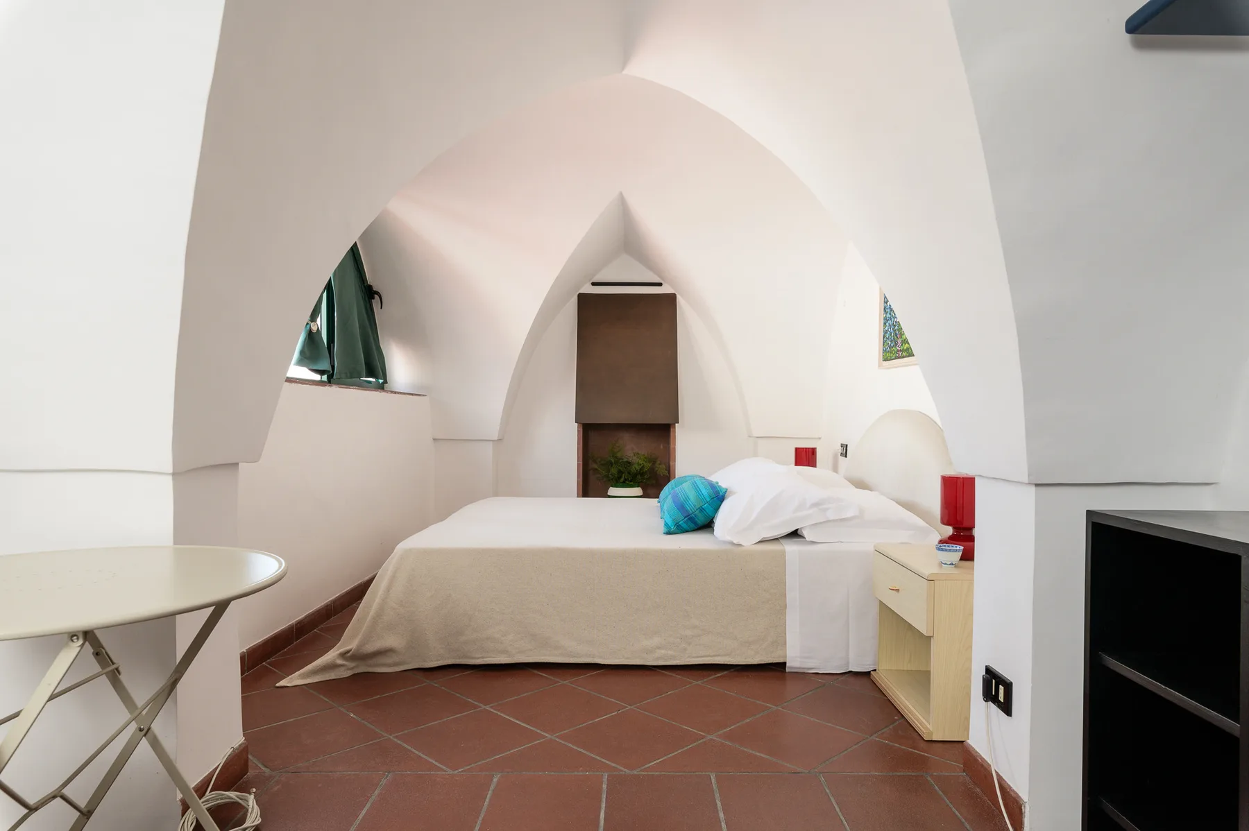 A bedroom with a bed beneath a broad arched ceiling.