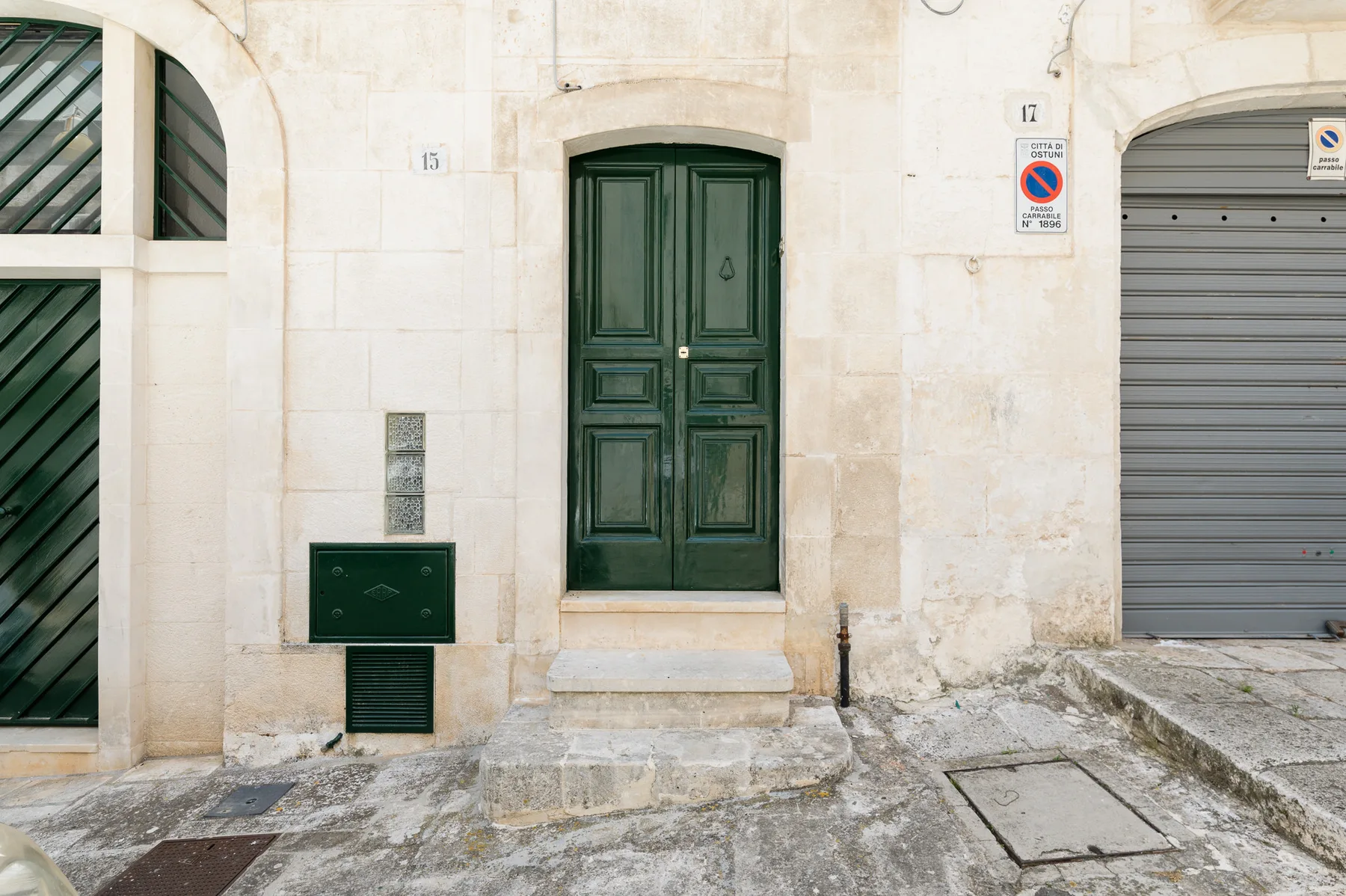 Fachada de piedra con una puerta doble verde oscuro y una persiana metálica gris.