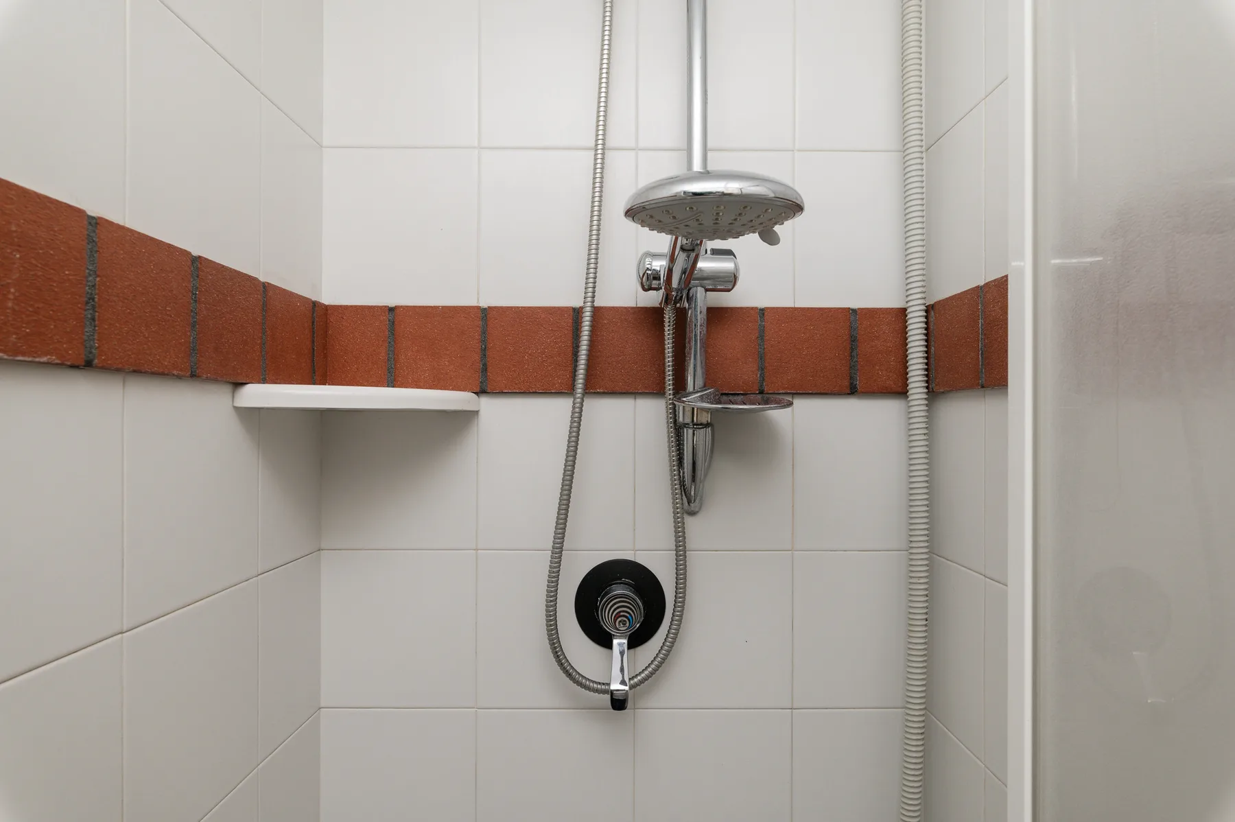 Una zona de ducha alicatada con un cabezal de ducha en la pared y una pequeña repisa.