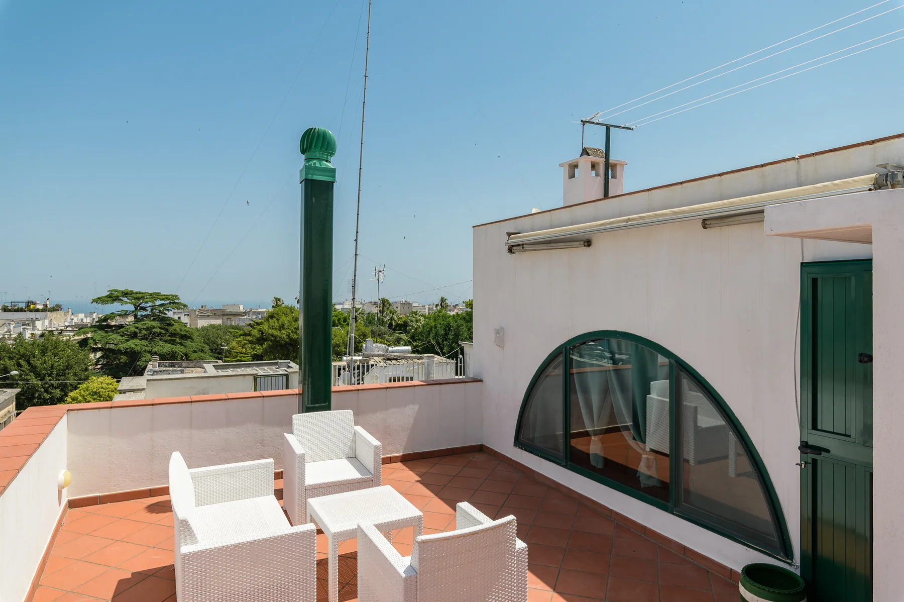 A sunny rooftop terrace with white seating beside a building with arched windows.