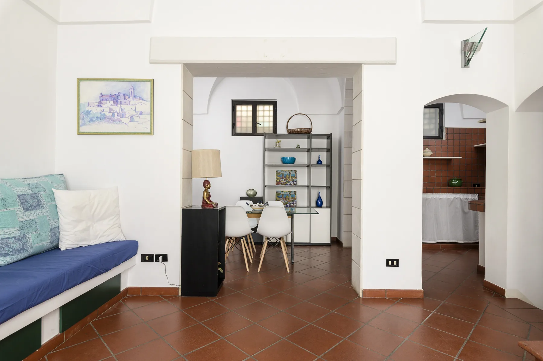 Una sala luminosa con escritorio integrado y asientos junto a una abertura arqueada hacia la cocina.