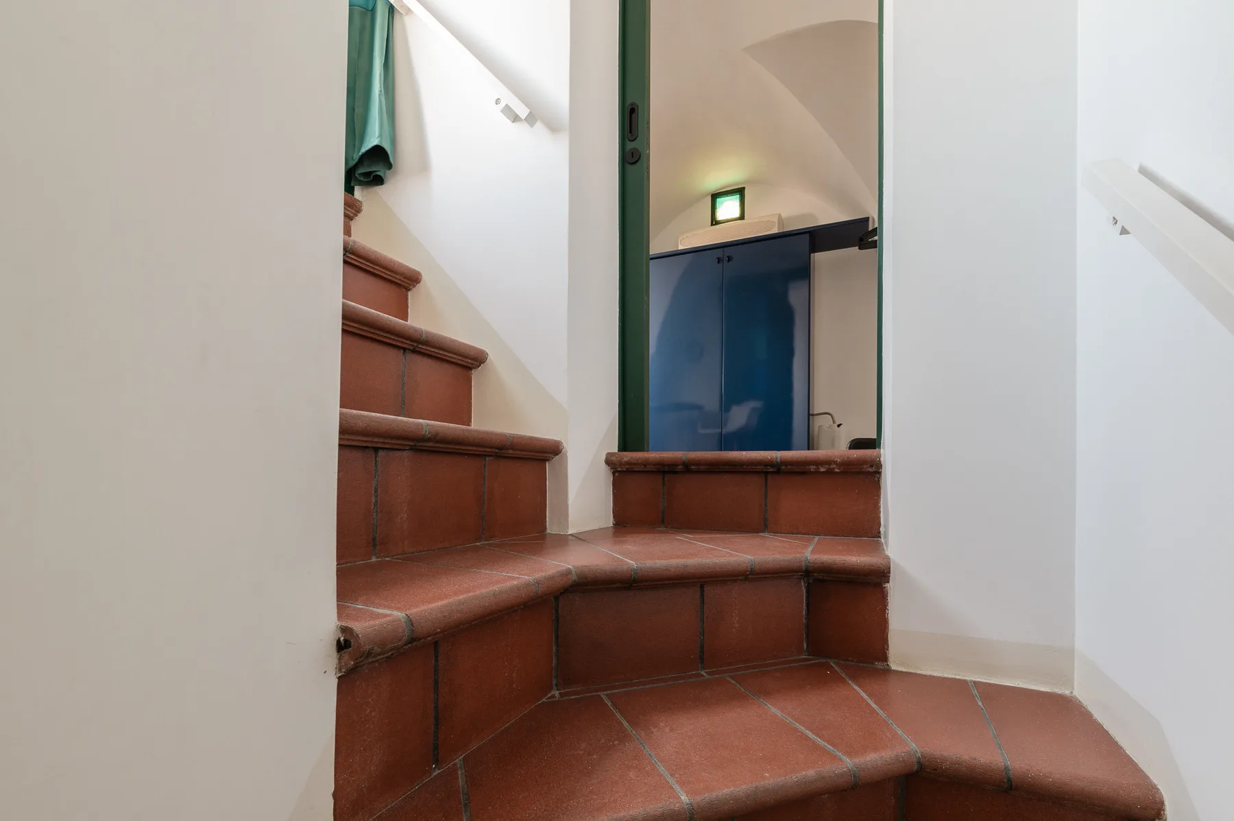 Una escalera de baldosas sube hasta una puerta junto a armarios azules.
