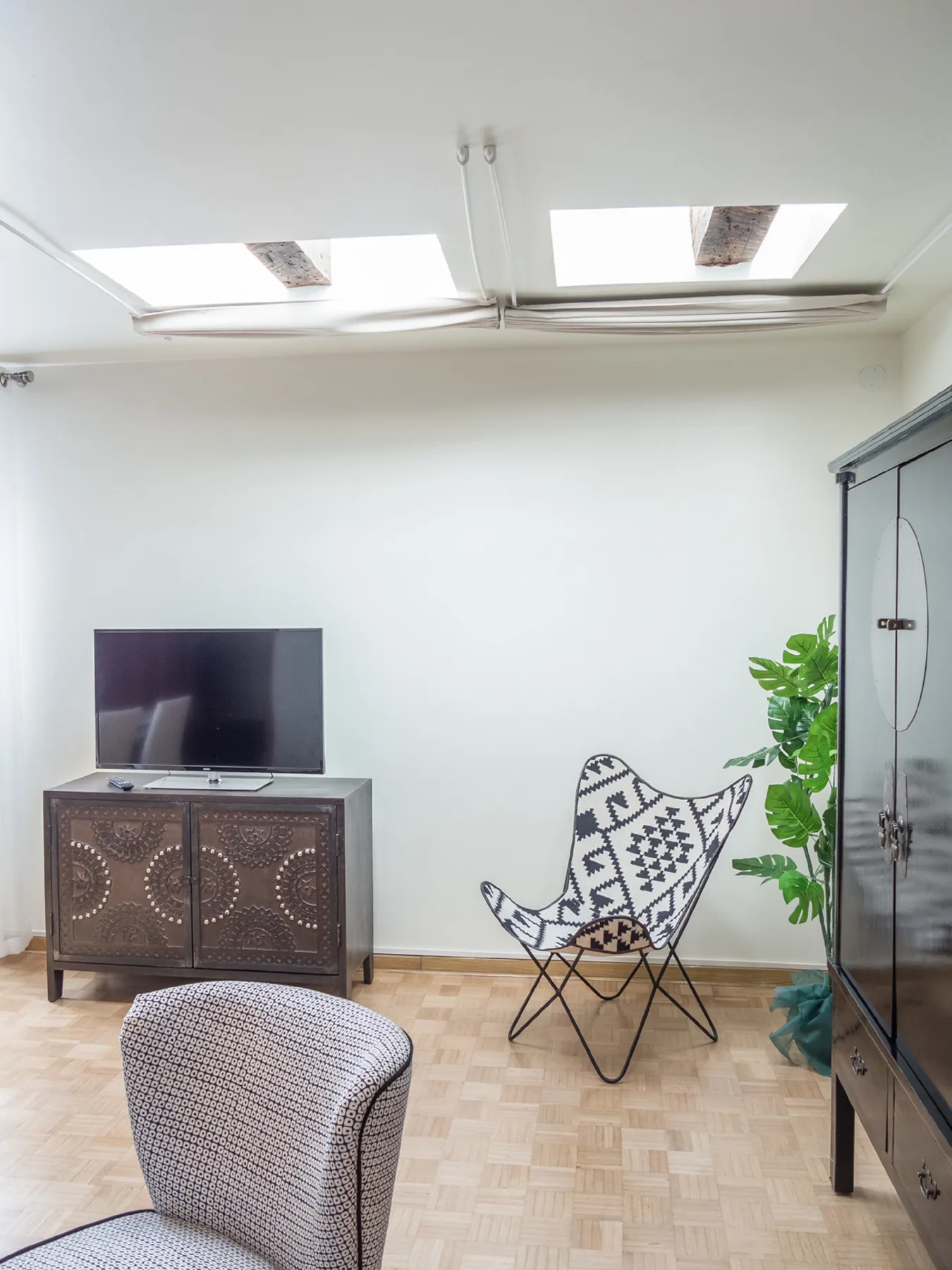A bright living area with a television, patterned seating, and a potted plant.