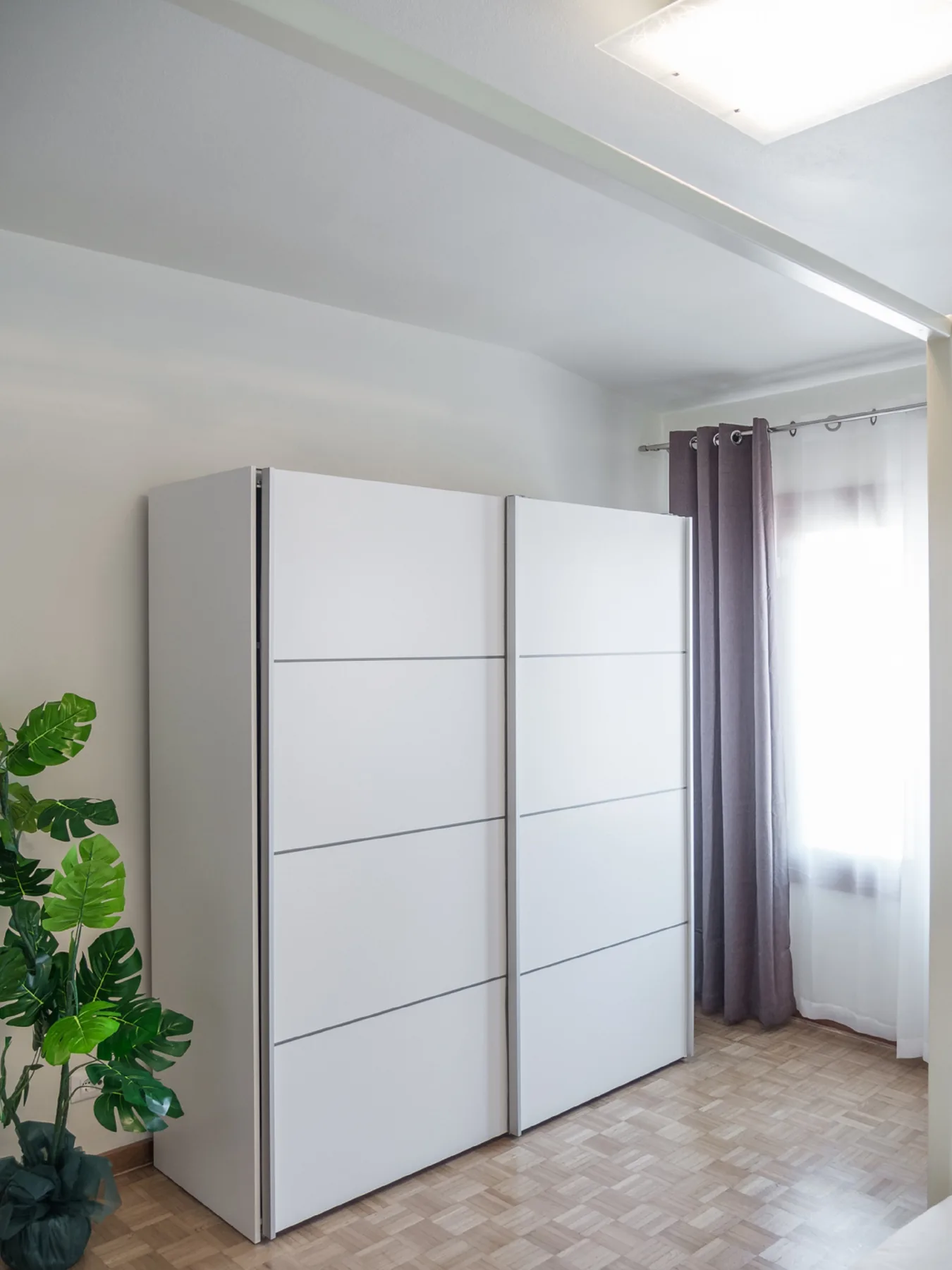 A bright room with a large white wardrobe beside a curtained window.