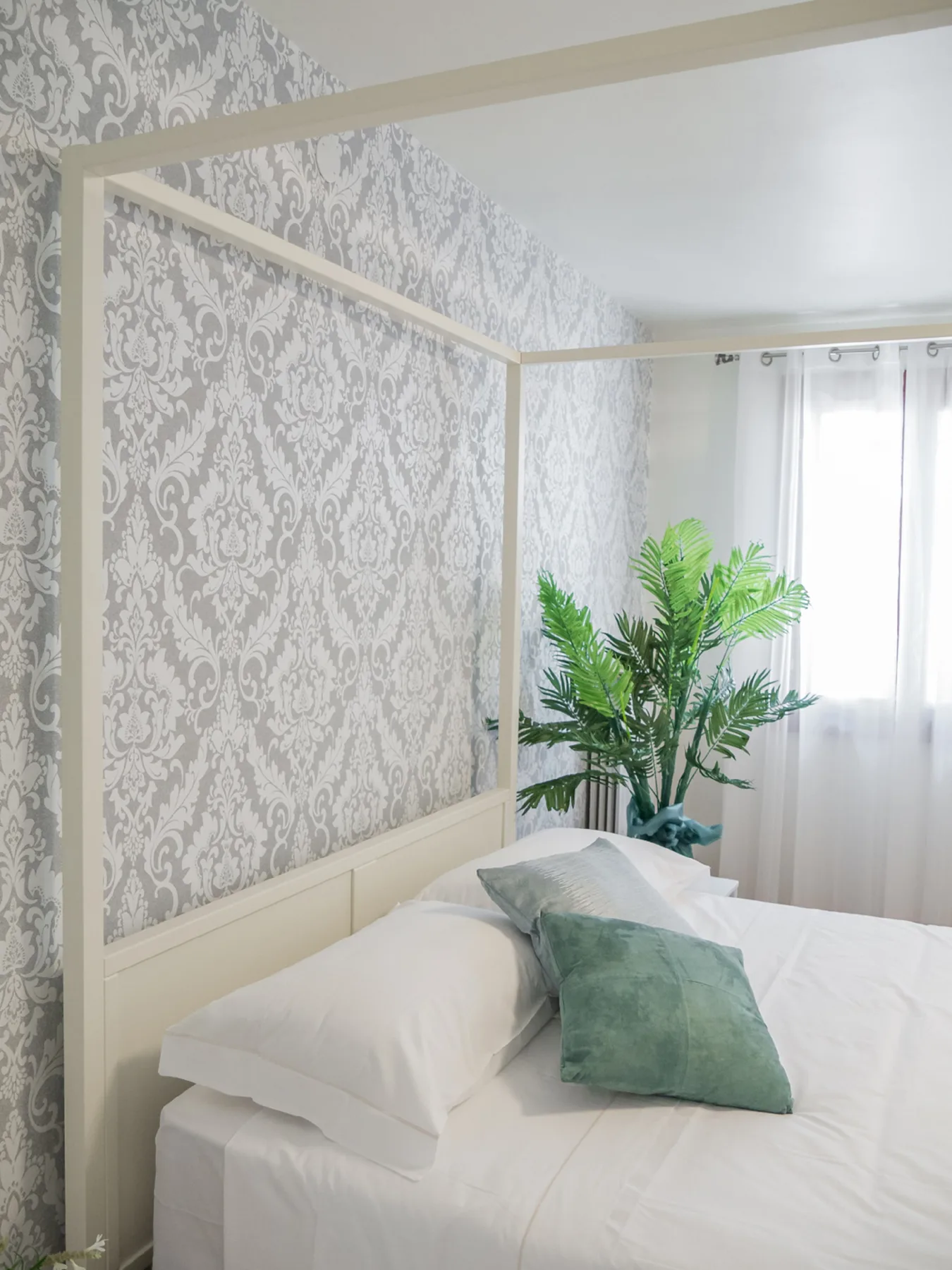 A bedroom with white bedding and a leafy plant beside the window.