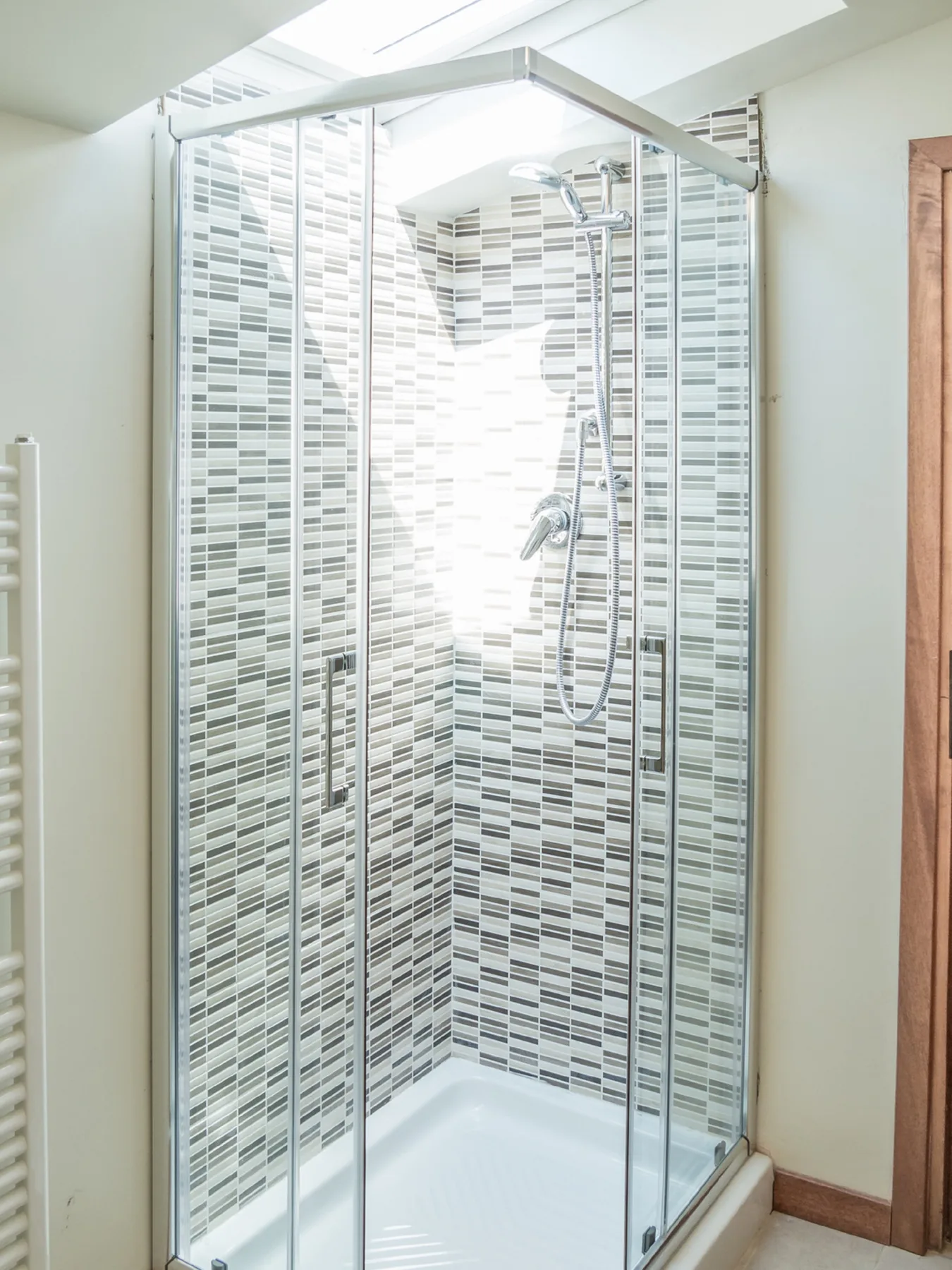 A bright bathroom shower with patterned tile walls and a glass enclosure.