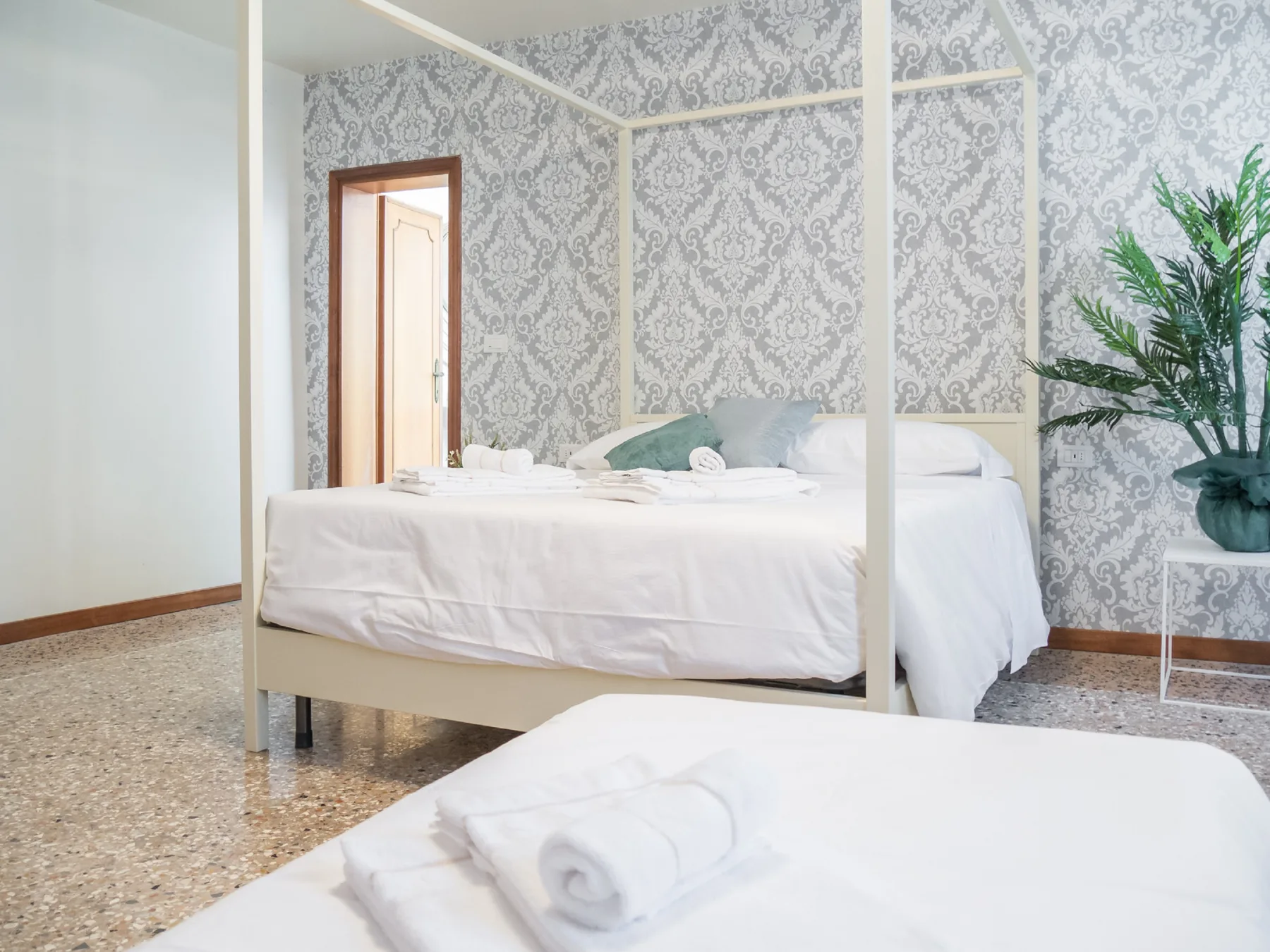 A bedroom with white bedding, patterned walls, and a leafy potted plant.