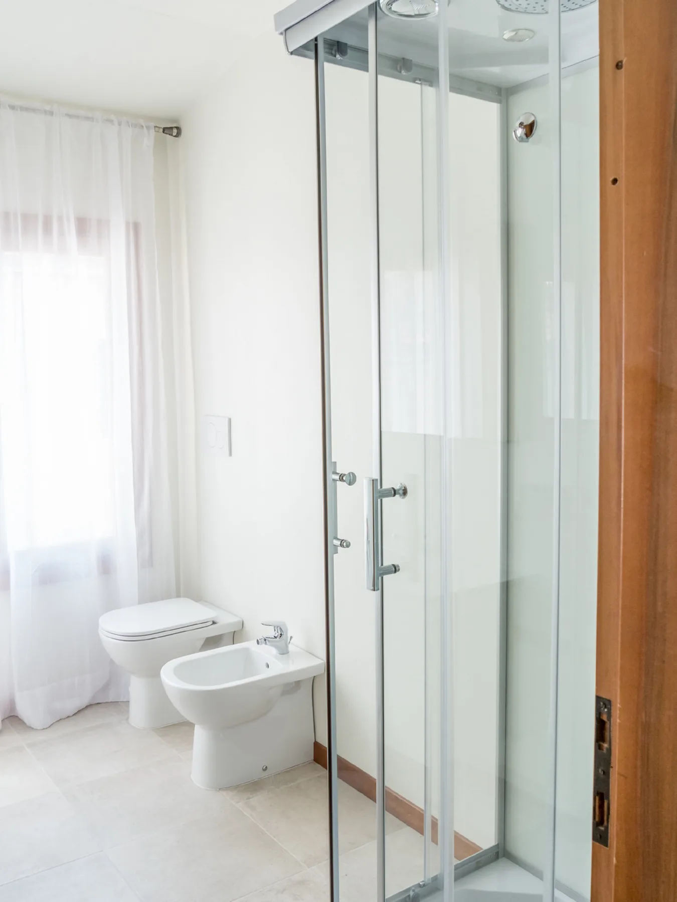 A bright bathroom with a glass shower, toilet, and bidet.