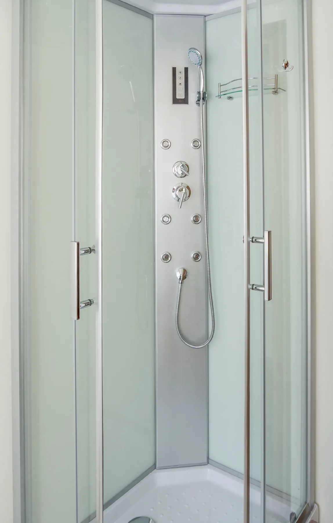 A glass-enclosed shower with a handheld showerhead and control panel.