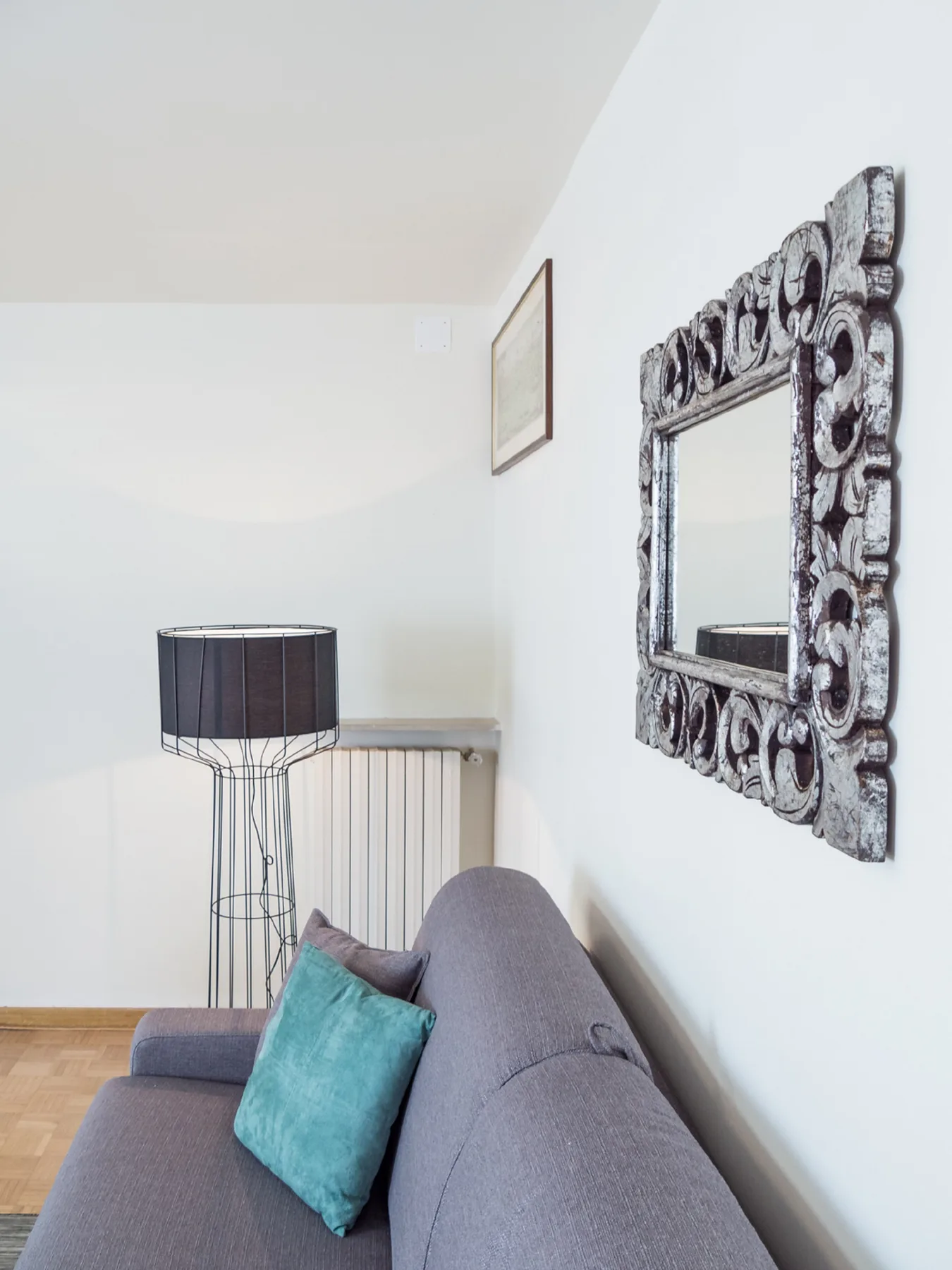 A bright living room with seating, a floor lamp, and an ornate wall mirror.