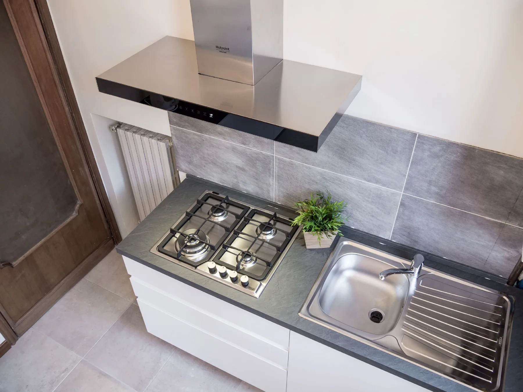 A compact kitchen with a cooktop, sink, and stainless-steel range hood.