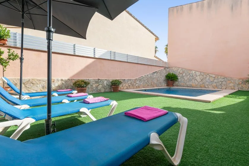 An outdoor pool area with blue loungers on green turf.
