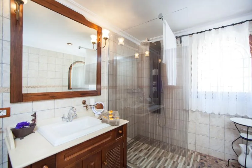 A tiled bathroom with a sink vanity, large mirror, and shower area.