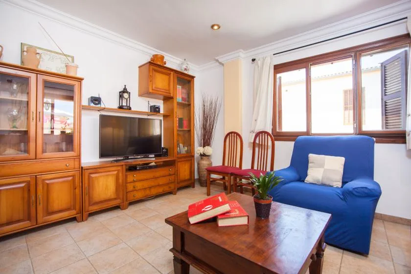 A living room with wooden cabinets, a television, and blue seating by the window.