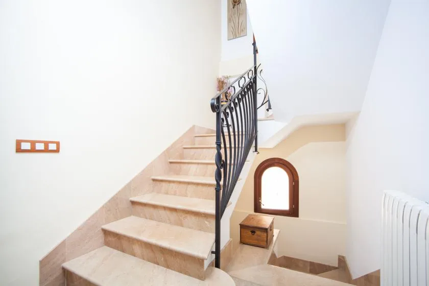 A bright indoor staircase with pale steps and a dark decorative railing.