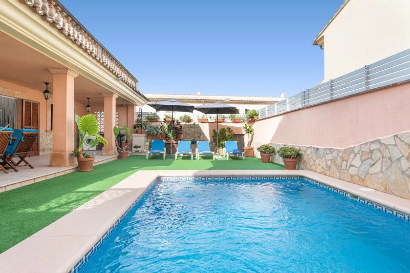 An outdoor swimming pool beside a patio with seating and potted plants.