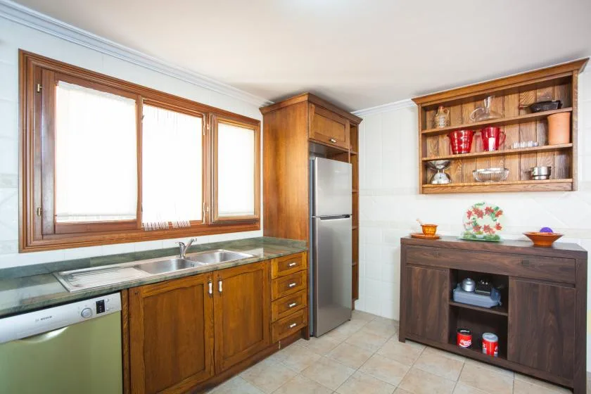 A kitchen with wooden cabinets, a refrigerator, and a counter beneath the windows.