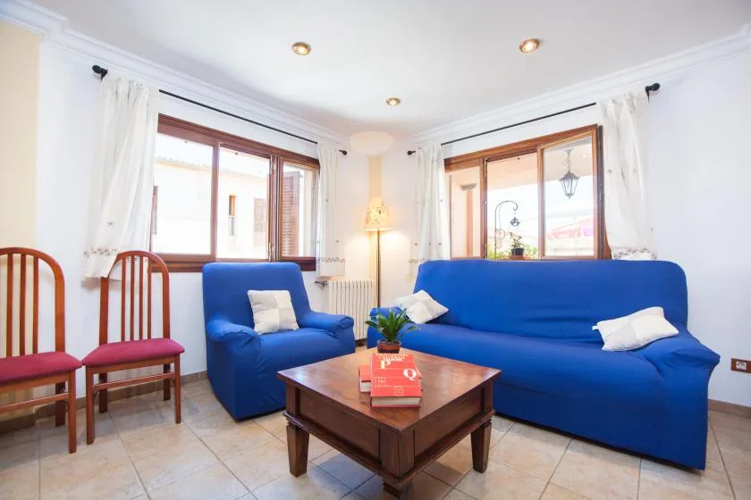 A bright living room with blue seating, wooden chairs, and a coffee table.