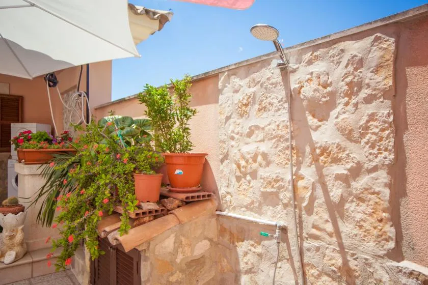 An outdoor shower beside a stone wall and a cluster of potted plants.