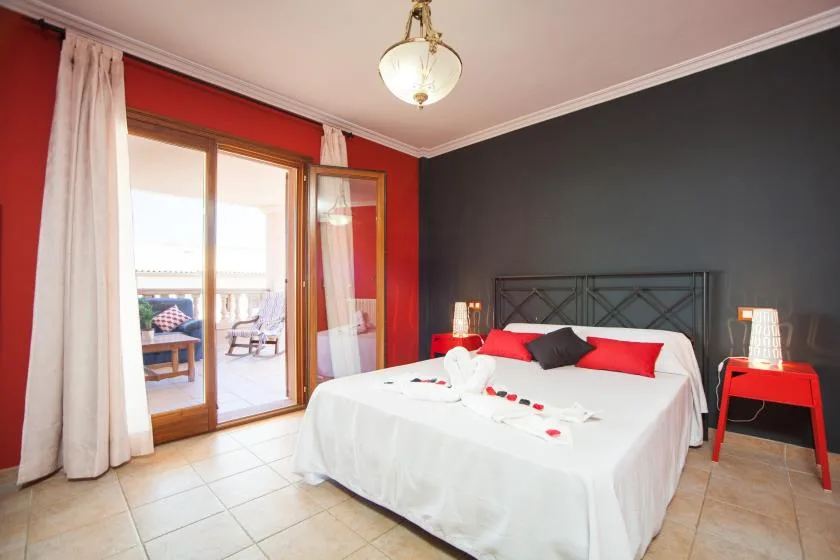 A bedroom with a white bed, red accents, and glass doors opening to a patio.